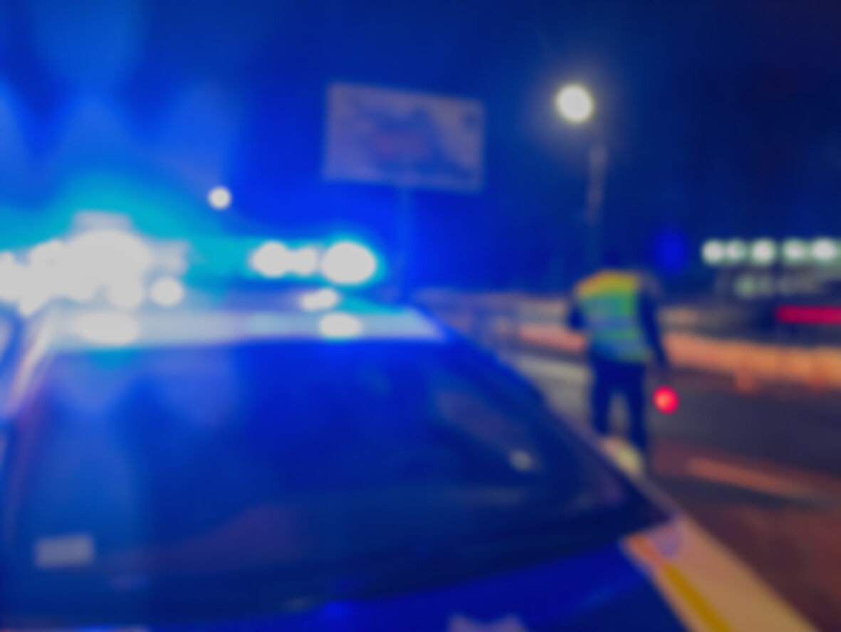 Blurred police car with flashing blue lights and an officer in the distance at night, symbolizing an incident with incomplete body cam footage.