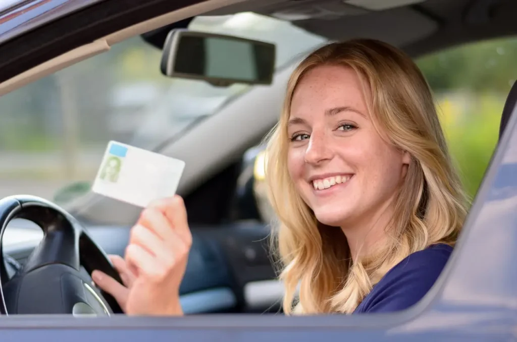 Smiling woman holding driver's license in car, symbolizing the license reinstatement process after suspension in Michigan.